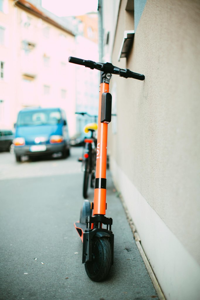 Vibrant orange electric scooter parked on a city sidewalk during daylight, showcasing urban transportation.