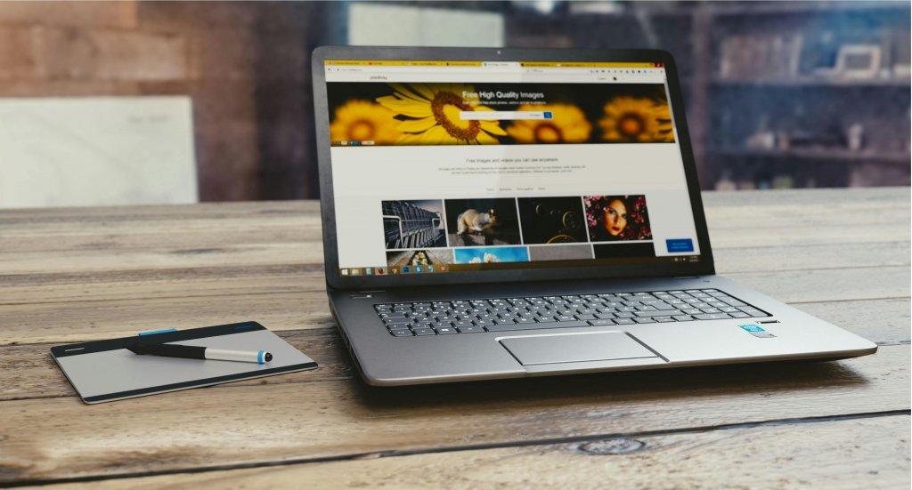 Laptop with open webpage on wooden desk, accompanied by tablet and pen, representing digital work setup.